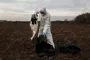 Mand i besjyttelsesdragt tager død stork i en sort affaldssæk