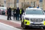 En masse bettjente foran en bygning og bag en parkeret politibil, der afspærrer vejen