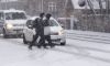 To personer går over en vej i snevejr mens bil holder tilbage