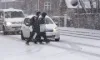 To personer går over en vej i snevejr mens bil holder tilbage