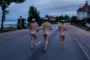 Bagsiden af tre nøgne mand med studenterhuer gående på en landevej